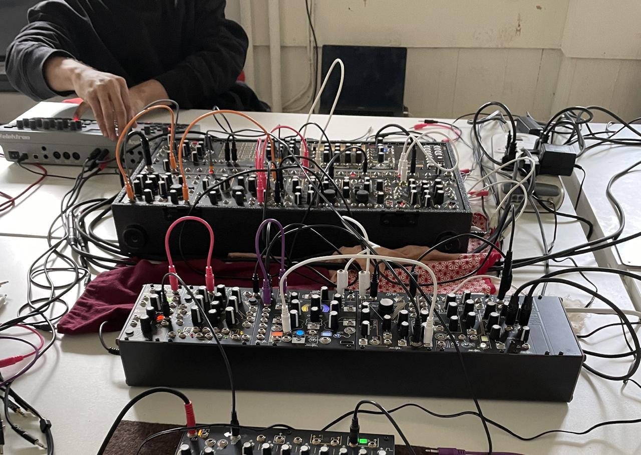 Two modular synthesizer cases on a table, covered in patch cables